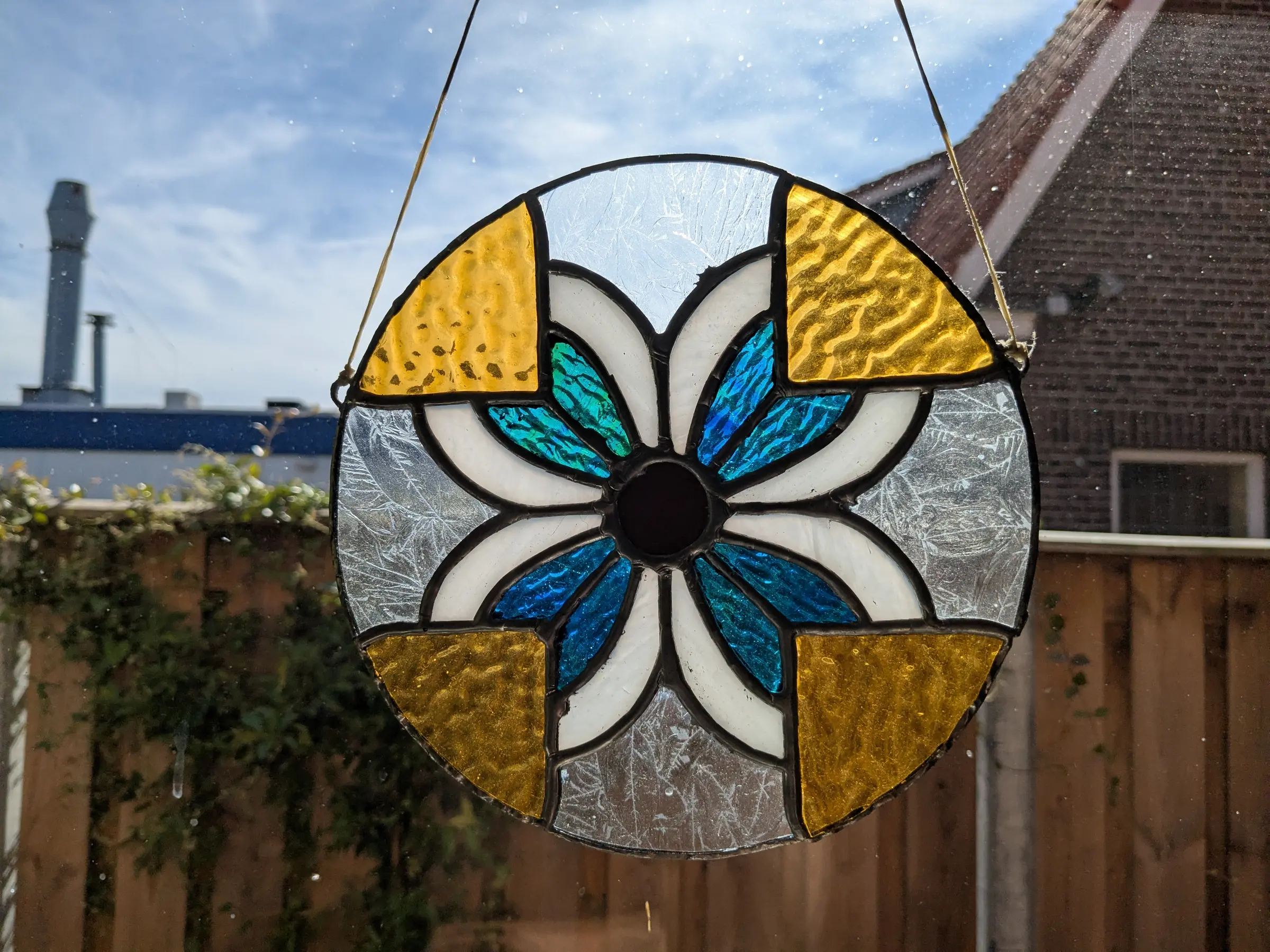 Rond glas-in-loodraam met bloemmotief in blauw, wit en goudgeel.