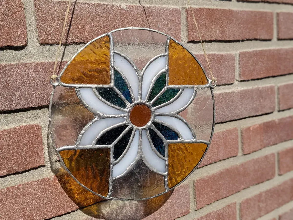 Rond glas-in-loodraam met bloemmotief in blauw, wit en goudgeel.
